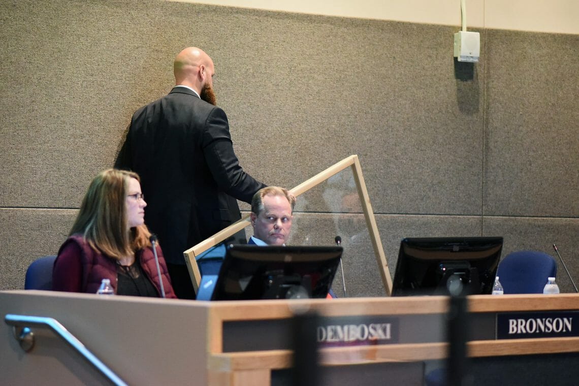 Adam Trombley removes the plexiglass shield from the podium where audience members provide testimony